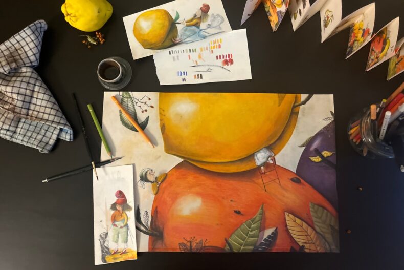 Künstlerischer Arbeitsplatz mit einer farbenfrohen Illustration von großen Früchten und kleinen Figuren. Umgeben von Buntstiften, Skizzen, einem Glas mit Pinselwasser und einem karierten Tuch.