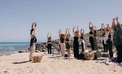 Menschen, die Bewegungsübungen an einem Strand machen. Das Meer ist im Hintergrund zu sehen.
