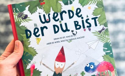 Ein bunt illustriertes Kinderbuch mit dem Titel „Werde, der du bist“ von Leni Koinegg, gehalten in einer Hand. Das Cover zeigt einen kleinen Wichtel, ein Chamäleon, einen Papagei und Blätter im Hintergrund.