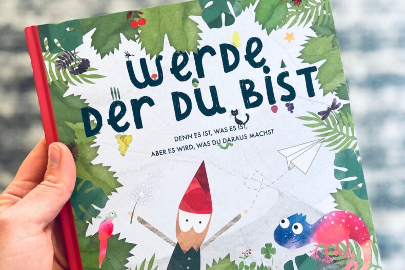 Ein bunt illustriertes Kinderbuch mit dem Titel „Werde, der du bist“ von Leni Koinegg, gehalten in einer Hand. Das Cover zeigt einen kleinen Wichtel, ein Chamäleon, einen Papagei und Blätter im Hintergrund.