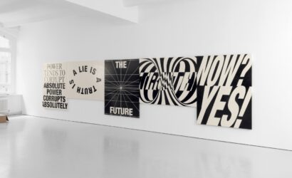 Sechs großformatige, schwarz-weiße Typografie-Plakate hängen nebeneinander an einer weißen Galeriewand. Die plakative Schrift zeigt Aussagen wie „POWER CORRUPTS ABSOLUTELY“, „A LIE IS A TRUTH“, „THE FUTURE“, „TRUTH“, „NOW?“ und „YES!“, teils in verzerrter oder perspektivischer Darstellung.