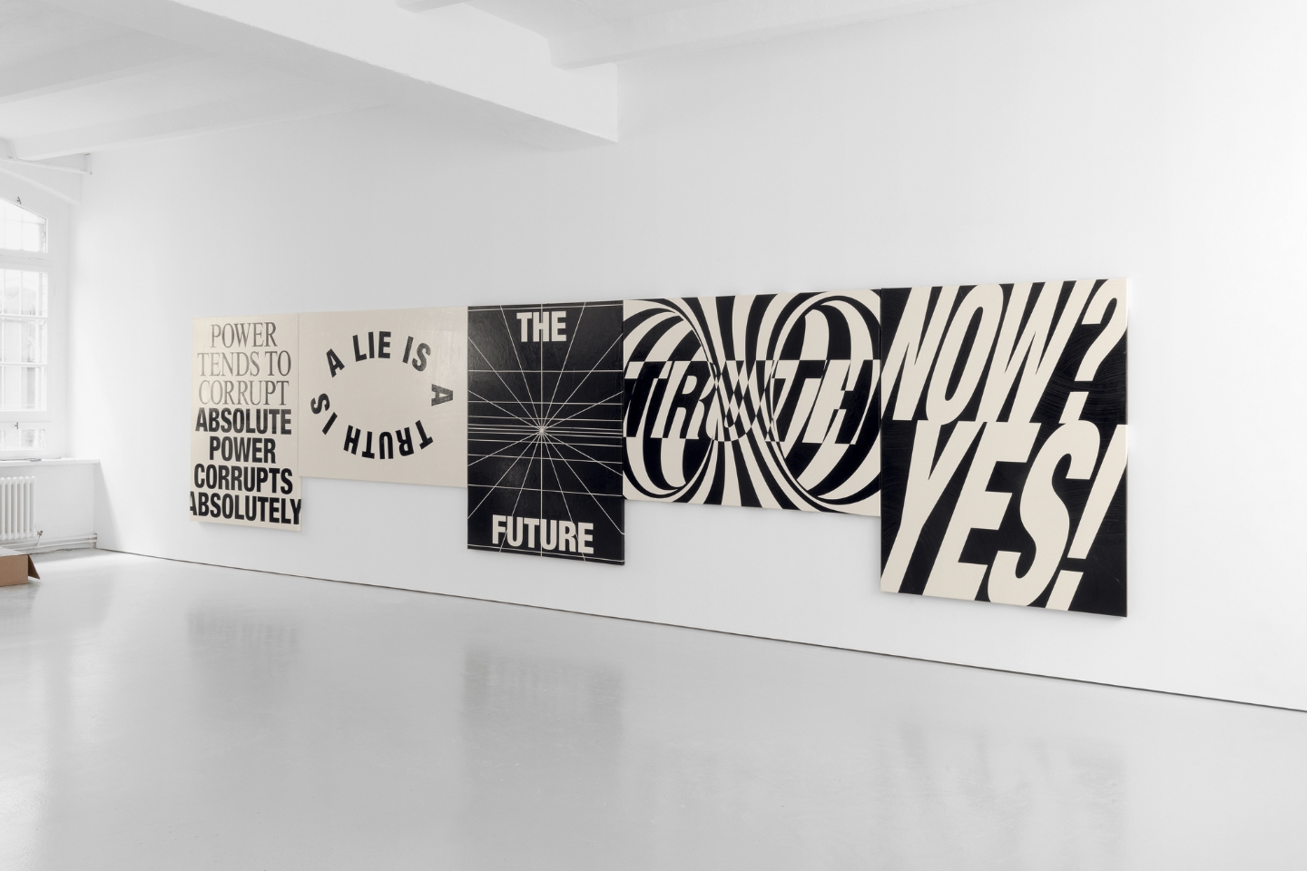Sechs großformatige, schwarz-weiße Typografie-Plakate hängen nebeneinander an einer weißen Galeriewand. Die plakative Schrift zeigt Aussagen wie „POWER CORRUPTS ABSOLUTELY“, „A LIE IS A TRUTH“, „THE FUTURE“, „TRUTH“, „NOW?“ und „YES!“, teils in verzerrter oder perspektivischer Darstellung.